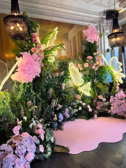 For an intimate gathering, we created this enchanting floral backdrop. A dense arrangement of pink flowers and greenery is accented with glowing neon butterfly lights, creating a magical and romantic photo space.