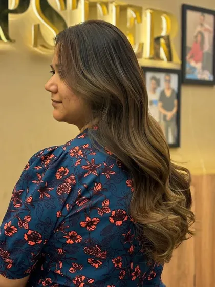 A beautiful balayage on long hair, with a seamless transition from dark roots to lighter ends, styled in soft, elegant waves.