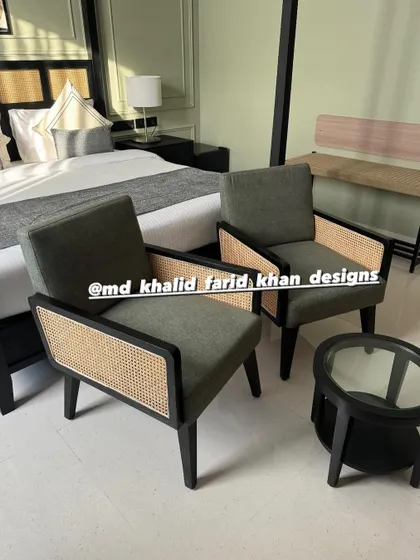 A close-up of the seating area in the hotel room, featuring two dark-framed armchairs with cane weaving and a matching circular side table.