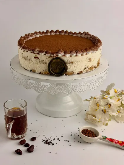 My classic Tiramisu, presented on a beautiful cake stand. It features layers of coffee-soaked ladyfingers and a rich, creamy mascarpone filling, generously dusted with cocoa powder.