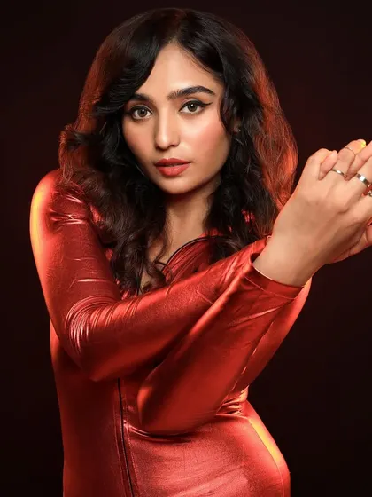A dynamic studio shot using a vibrant red outfit and warm, smoky background to create a sense of energy and movement. The lighting highlights the metallic texture of the fabric.