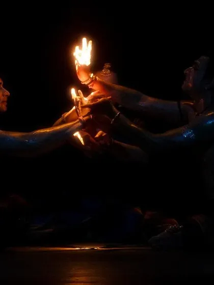 A scene from 'Naga Mandala' where the dancers' hands, holding small lights, come together to create a larger flame. This is a key visual in the production.