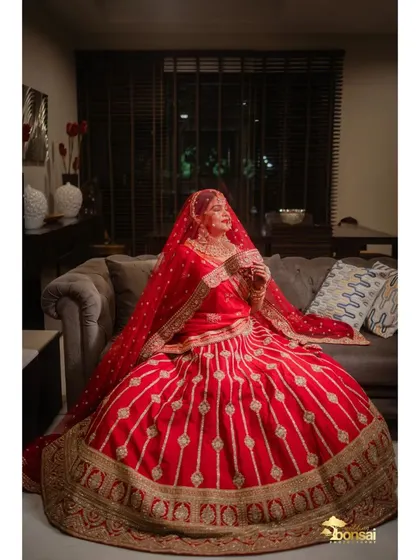 A seated portrait of the bride, showcasing the volume and detail of her wedding lehenga.