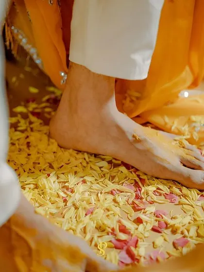 A detail shot focusing on the feet standing in a bowl of flower petals and turmeric, an artistic view of the Haldi ceremony's elements.