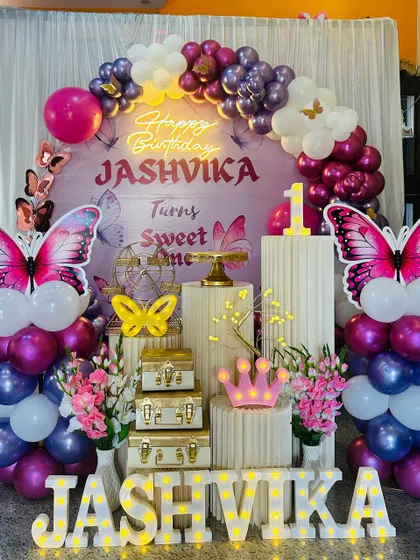 A vibrant butterfly themed first birthday party. This setup features large pink butterfly wings, a custom backdrop, and marquee letters spelling out the name.