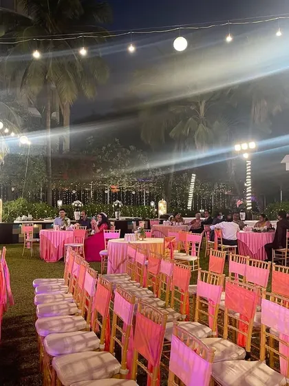 A beautiful pink-themed seating arrangement for an outdoor reception. The lawn is filled with elegantly decorated tables under a canopy of glowing lanterns.