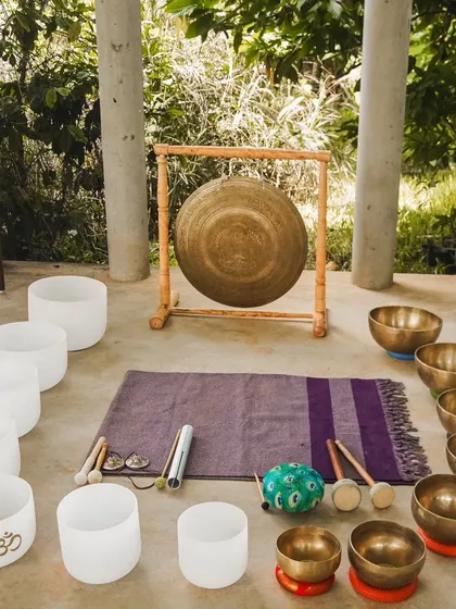 A beautiful setup of instruments in nature, ready for a transformative sound bath. This arrangement includes crystal bowls, Tibetan bowls, a gong, and chimes, blending their vibrations with the peaceful energy of the outdoors.