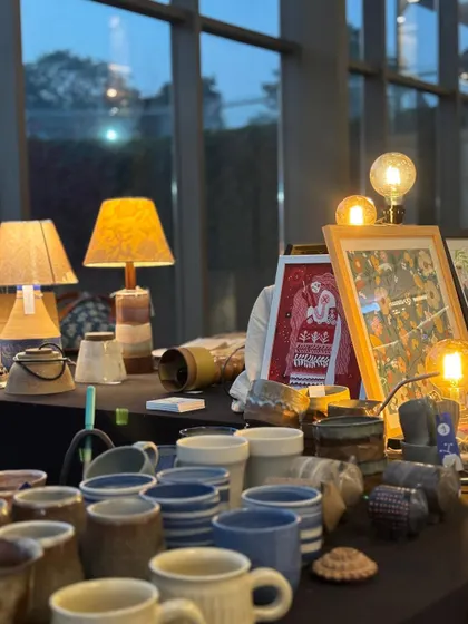 A view of our market stall, with the warm glow of our handmade lamps and a collection of mugs and tumblers.