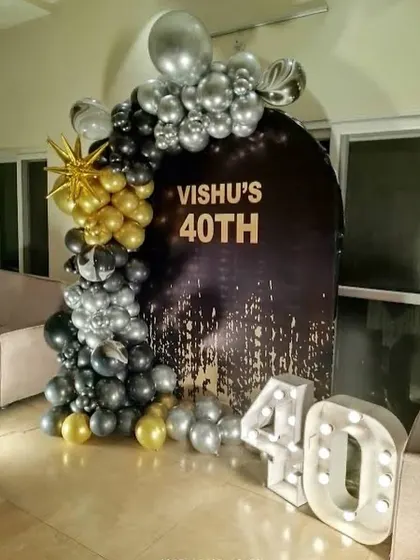 A sophisticated 40th birthday with a black, silver, and gold theme. This setup includes a personalized backdrop, a balloon arch, and light-up numbers.