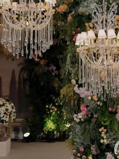 A detail shot of the lush greenery and floral arrangements climbing the pillars of the ceremony structure, with crystal chandeliers adding a touch of sparkle.