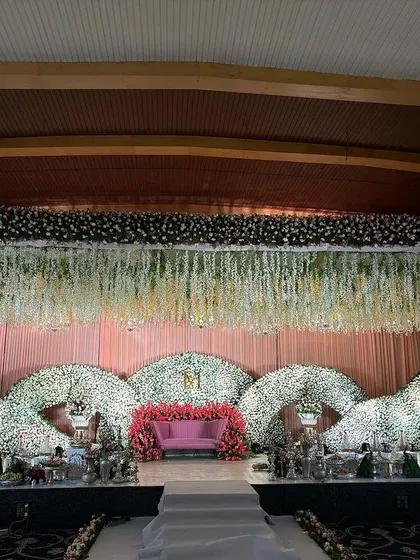 A beautiful stage with three large, curved floral structures made of white flowers, creating a soft and elegant backdrop.