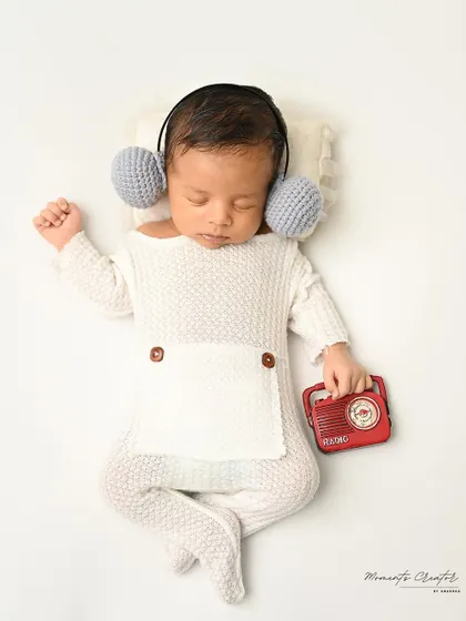 Lost in the music. This newborn, dressed in a simple white outfit, sleeps with tiny headphones and a miniature radio.