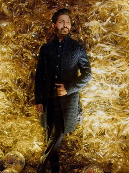 The groom looking dapper and confident against the gold foil backdrop, showcasing his stylish Sangeet attire.
