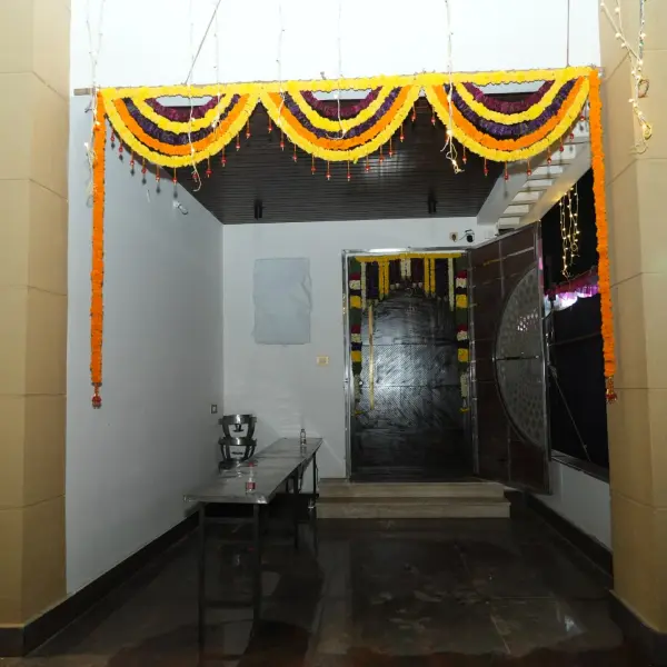 A deep marigold toran in yellow, orange and maroon across an entrance passage, with string lights at the sides and a garlanded door at the far end