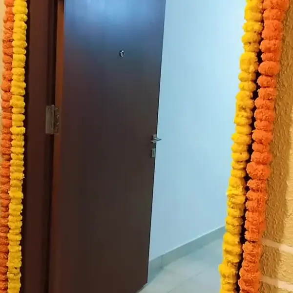 A flat's front door at a housewarming, framed in strings of orange and yellow marigold, with a marigold swag across the top