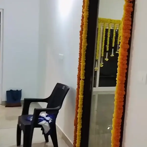 An inside door frame in an empty flat wrapped in a double string of orange and yellow marigold, with a plastic chair beside it and a marigold curtain seen through the door