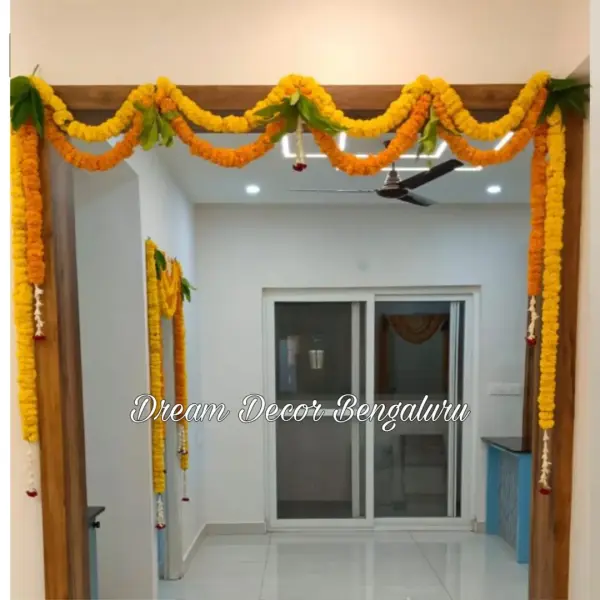 An inside doorway in a new flat at a housewarming, framed with yellow and orange marigold strings and mango leaves, with more marigold on a second doorway behind