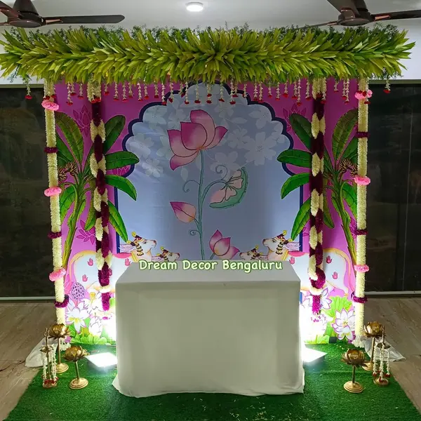 A ceremony backdrop with a printed lotus panel, framed by strings of artificial flowers and a fringe of green leaves