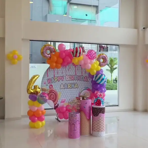 A candy fourth birthday in a clubhouse: a round print reading Happy Birthday Aarna with drips and sweets, a pink, orange and yellow garland with donut and candy foils, ice-cream-cone plinths and a gold 4 on a balloon column