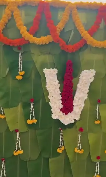 A wall of whole banana leaves with swags of orange and red marigold along the top, a namam in white flowers with a red centre, and small yellow and white flower drops