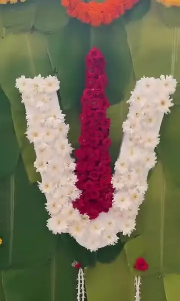 A namam in white flowers with a red centre on a wall of banana leaves, under a swag of orange marigold, with small flower drops