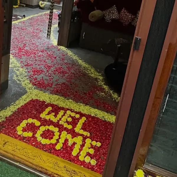 WELCOME spelt in yellow marigold petals on a bed of red rose petals at a doorstep, with a path of petals into the house and yellow and white garlands on the door frame