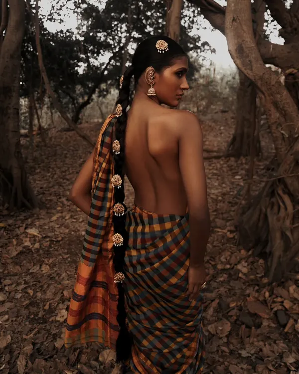 A portrait from an outdoor editorial, set against the rich textures of banyan tree roots. The earthy tones and natural setting create a raw and powerful image that feels deeply connected to nature.