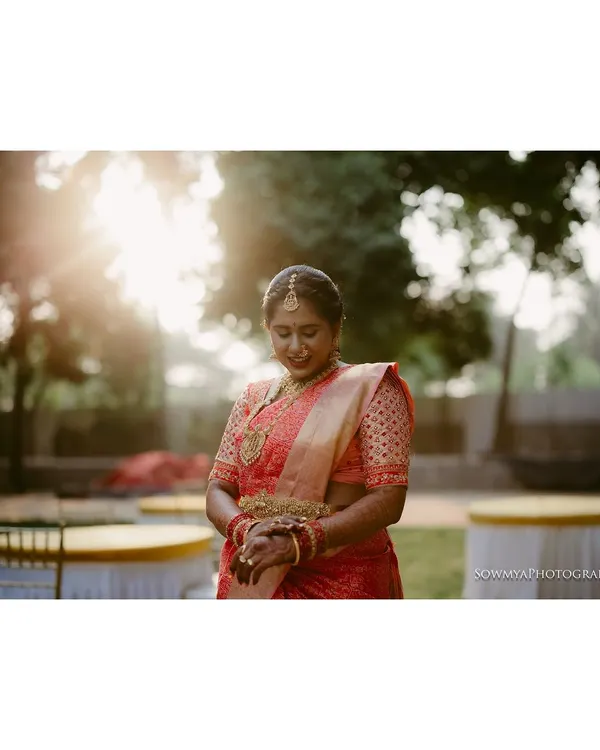A serene bridal portrait captured in the soft morning light. The bride, in her beautiful red saree, is having a quiet moment of reflection before the ceremony begins.