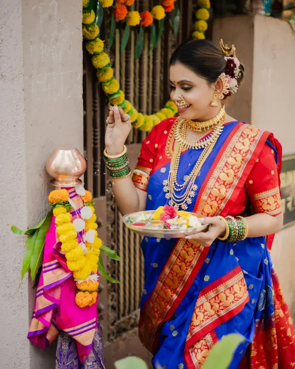 Celebrating the Maharashtrian new year with a traditional Gudi Padwa shoot. This image captures the model performing the puja, dressed in a stunning blue and red Paithani saree, surrounded by festive decorations.