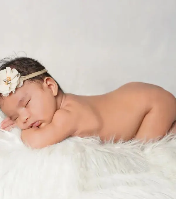 The classic newborn pose. This baby is sleeping peacefully on a soft white fur rug, a simple and timeless portrait that highlights their delicate form.