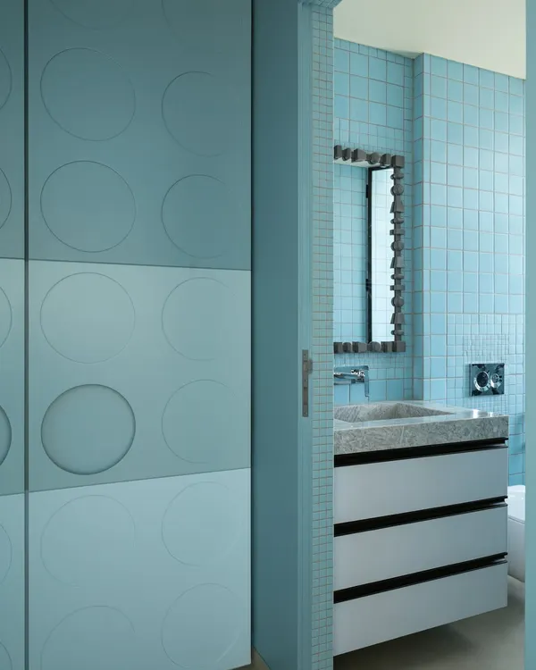 A glimpse into a bathroom designed for one of the sons in a family home. The space features a custom stone vanity with clean lines, paired with a playful circular-motif wardrobe just outside, blending sophistication with a touch of whimsy.