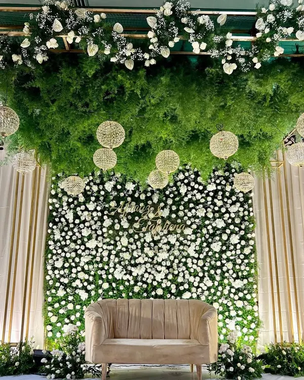 This reception stage is one of our absolute favorites. We created a lush ceiling of fresh greenery and hanging floral spheres over a wall of white flowers, designing a dreamy, elegant space for the couple's special evening.