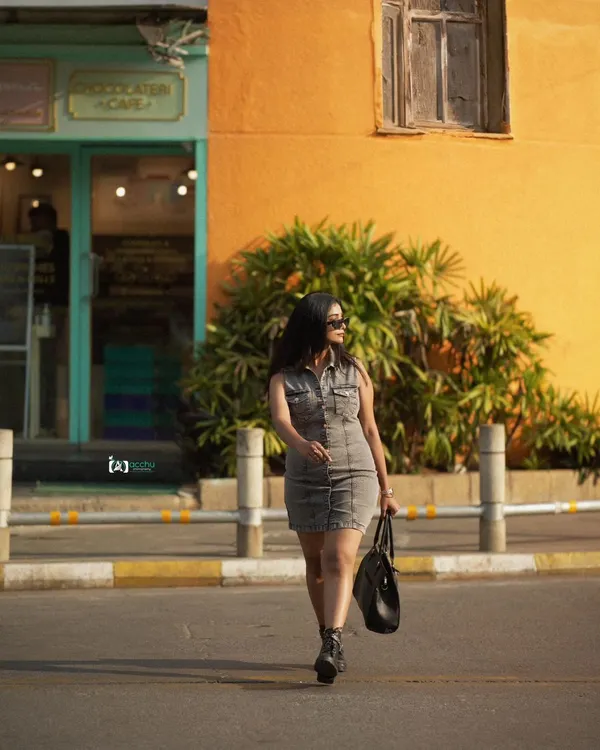 A candid-style street shot. The subject is captured mid-stride, creating a sense of movement and purpose. The warm, yellow wall provides a vibrant backdrop for this urban fashion portrait.