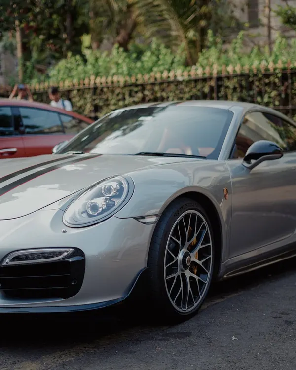 A sleek silver Porsche 911 with black racing stripes, parked on a city street. This shot captures the aggressive lines and high-performance look of a modern supercar.