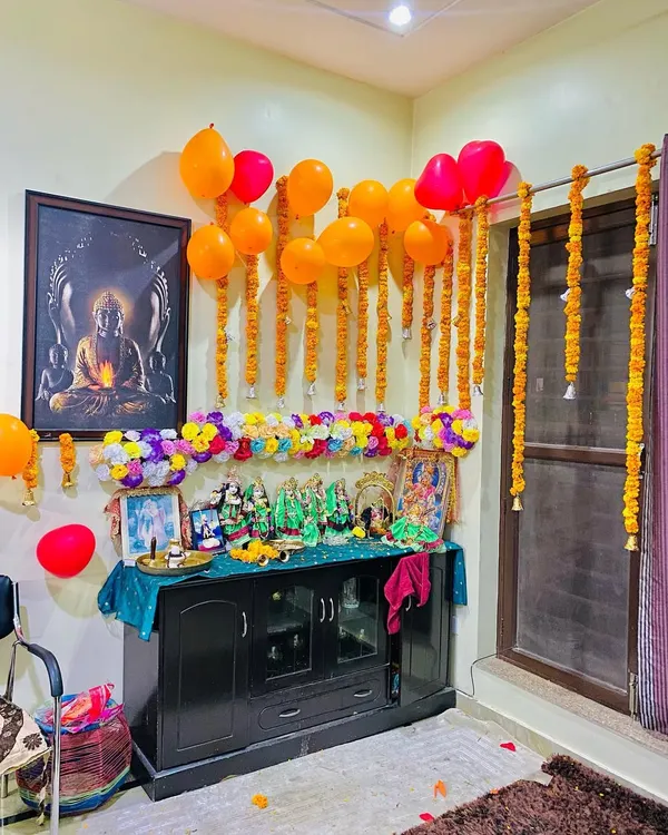 A home pooja corner decorated for a celebration. I used hanging marigold garlands and a line of colorful artificial flowers above the deities, along with some balloons for a festive touch.