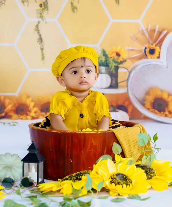 Our sunflower theme is perfect for a bright and cheerful photoshoot. This little one looks adorable in a yellow outfit, sitting in a wooden bucket surrounded by sunflowers.