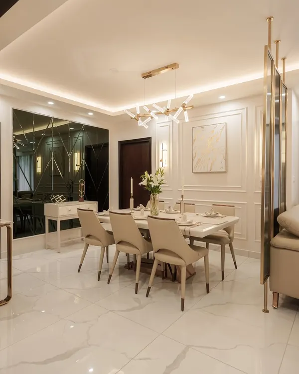 This elegant dining area at DNR Arista features a stunning marble-top table and comfortable upholstered chairs, set against a backdrop of classic wall molding. The modern chandelier and reflective wall partition add layers of light and luxury, creating an ideal setting for both intimate meals and grand celebrations.