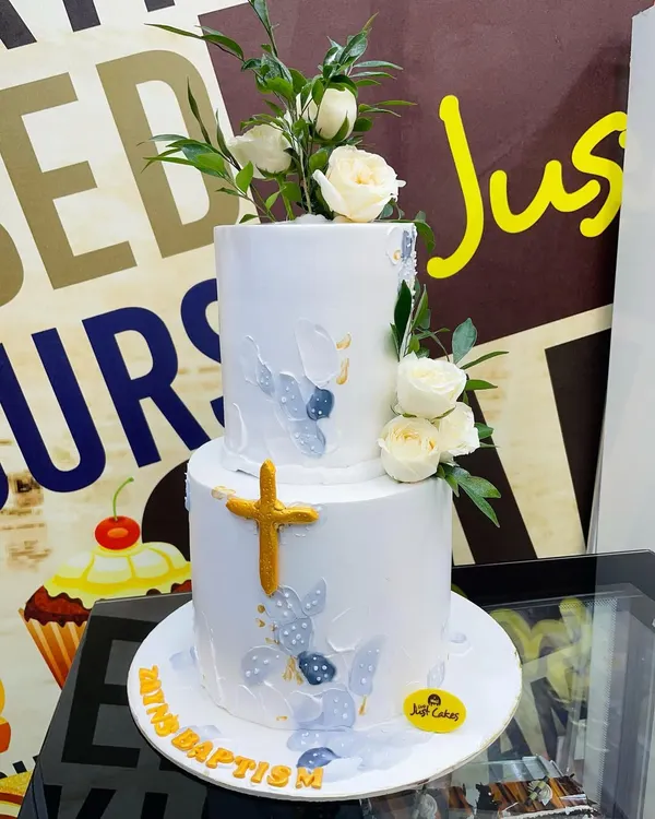 A stunning 5kg two-tiered Baptism cake in white, decorated with delicate fresh roses, subtle blue and grey painted details, and a golden cross.