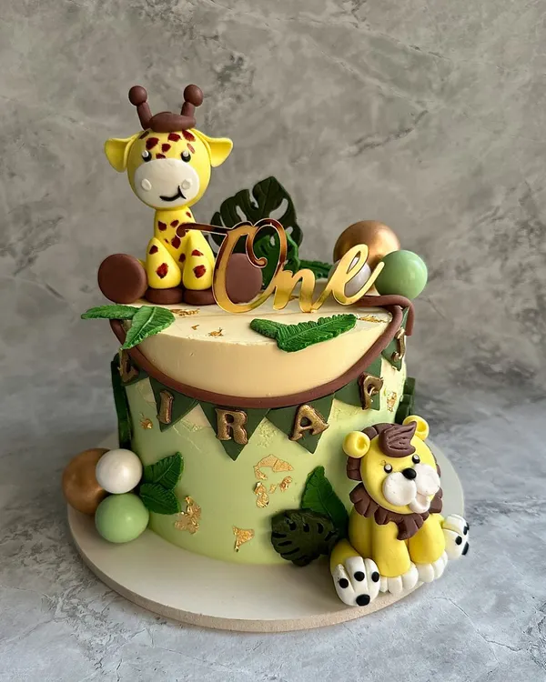 A wild first birthday adventure! This jungle-themed cake features hand-modeled fondant animals, including a friendly giraffe and lion, set against a backdrop of edible leaves and gold accents.