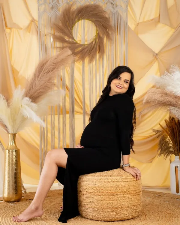 A relaxed and happy solo portrait in our boho studio. The mom-to-be, dressed in a simple black dress, smiles warmly, capturing a moment of pure contentment.
