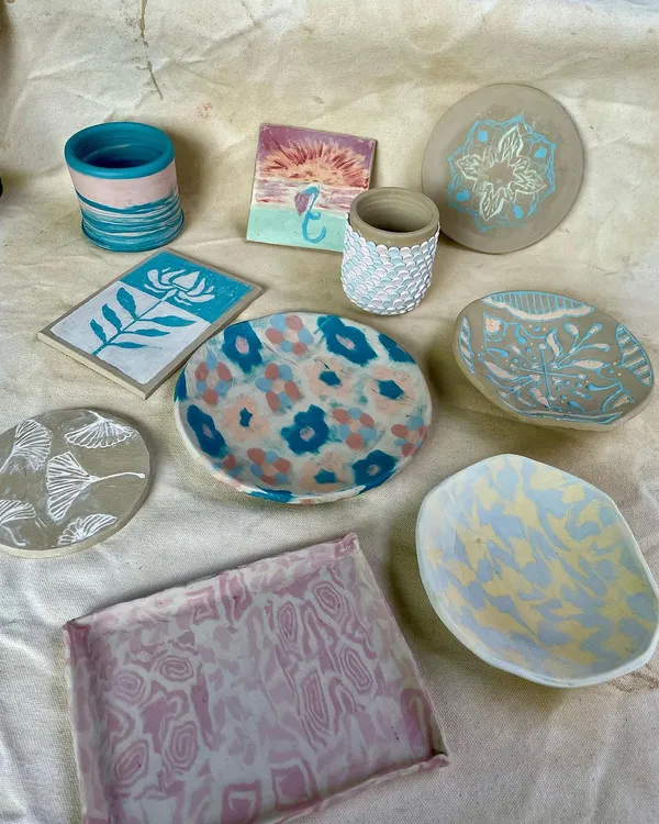 A beautiful flat lay of finished student work from various courses. You can see a variety of techniques, including painted plates, carved coasters, and textured cups.