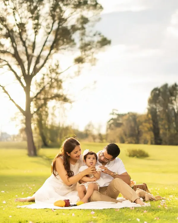 A sweet family picnic moment captured in warm, golden sunlight. This candid shot shows the parents lovingly interacting with their baby, creating a memory filled with tenderness and natural beauty.