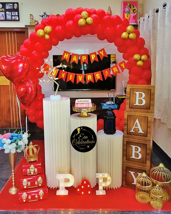 A classic red and gold anniversary setup for a celebration at home. It features a red balloon arch, white plinths for the cake, and marquee letters.