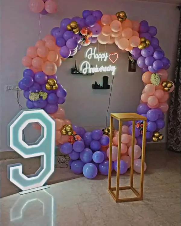 For this 9th anniversary, I created a beautiful circular balloon arch using purple, peach, and gold balloons. The setup includes a 'Happy Anniversary' neon sign and a large light-up number '9' to mark the special occasion.
