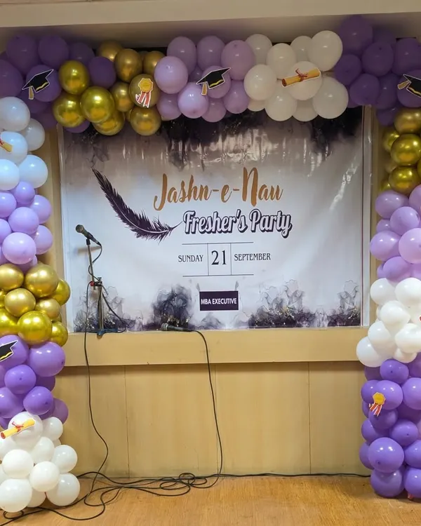 This is a complete stage setup I designed for a college fresher's party. It features a custom backdrop with the event name, "Jashn-e-Nau," and a full balloon arch in purple, white, and gold, accented with graduation cap cutouts to match the academic theme.