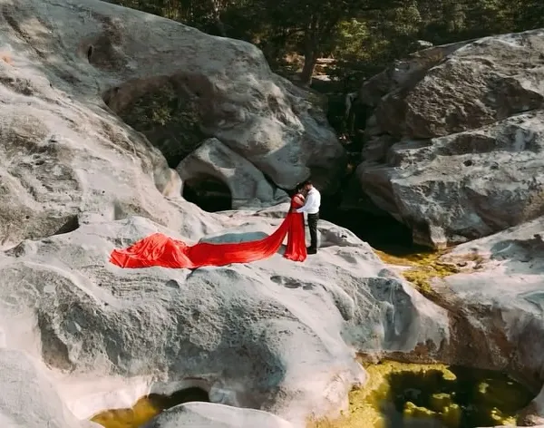 An aerial view showcasing the sheer drama of our red infinity trail gown. The vibrant color pops against the natural rock formations, creating a breathtaking shot for any couple.
