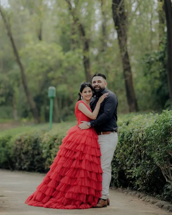 A classic portrait from an engagement shoot in a lush Pune garden. The woman's striking red gown and the couple's confident pose create a timeless and elegant image, showcasing a more formal and styled approach to pre-wedding photography.