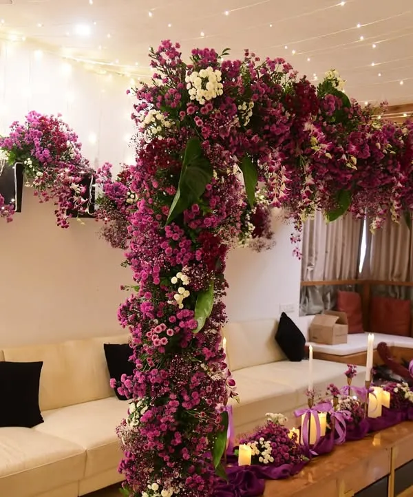 This stunning floral arch, created in a deep purple and magenta palette, became the centerpiece of the living room for a special celebration. It's paired with a matching table runner and fairy lights.