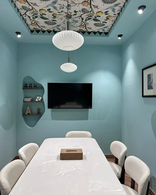 A view of our newly revamped studio's meeting room. The space features calming blue walls, a ceiling with floral wallpaper, and a large marble-finish table for client consultations.