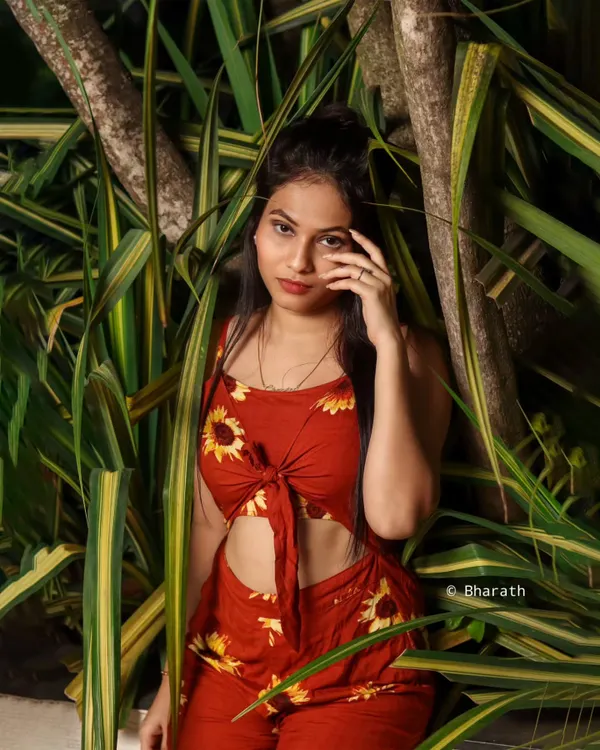An outdoor portrait using dense, leafy foliage as a natural backdrop. The vibrant greens make the subject's red outfit pop.